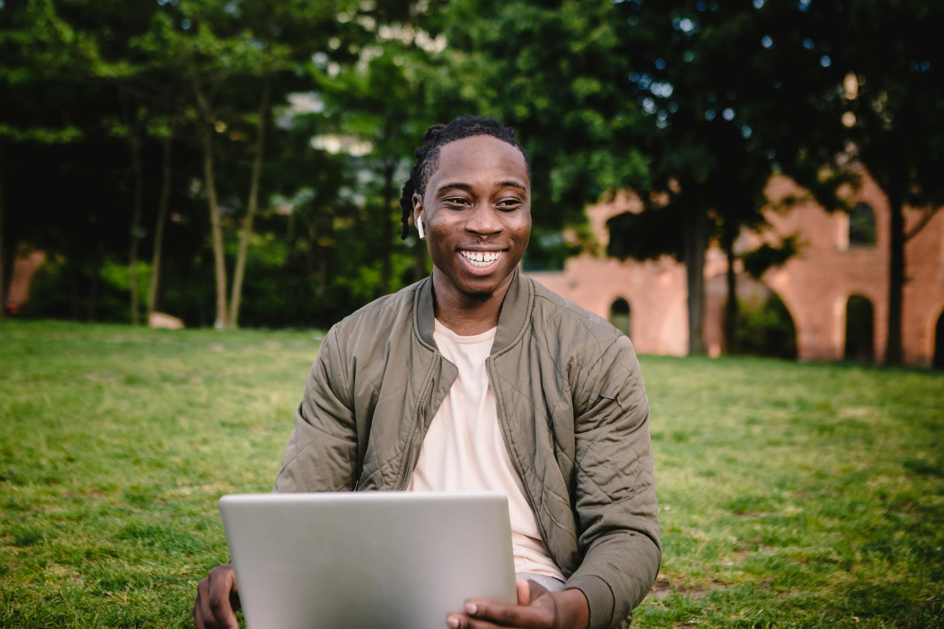 cheerful man with laptop and wireless earphones in park