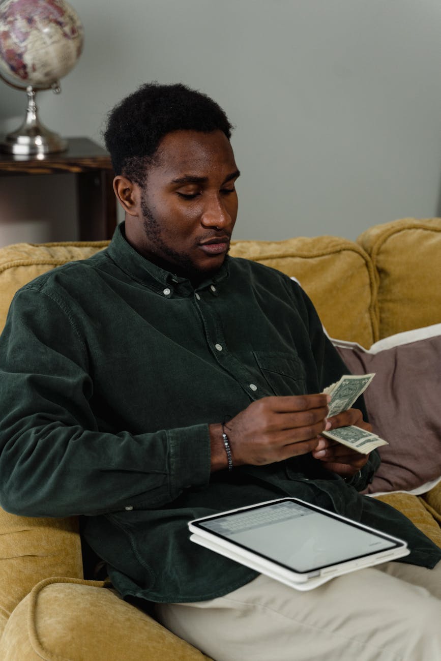 a man in black long sleeves counting his money while sitting on the couch