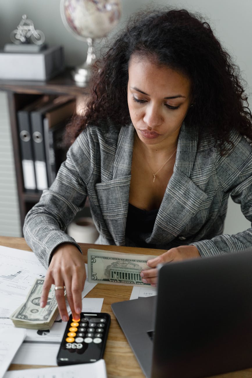 a woman in plaid blazer using her phone calculator while holding dollars