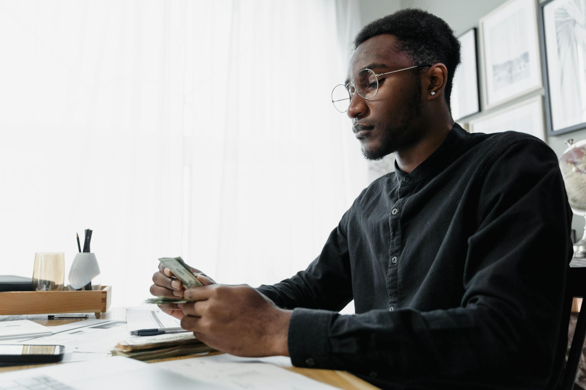 man in black long sleeves wearing eyeglasses while holding paper money