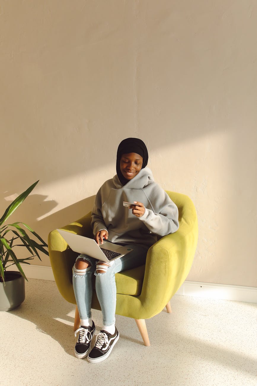 woman sitting on sofa chair while holding a laptop and a credit card