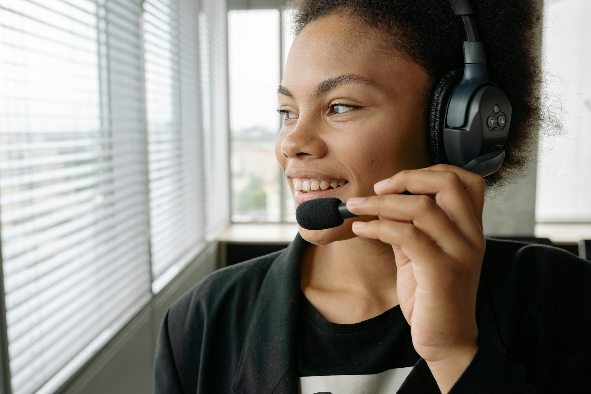 close up photo of a woman with curly hair holding the microphone of her headset